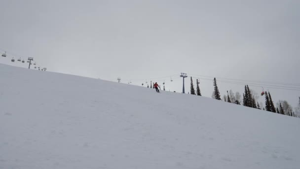 Επαγγελματίας σκιέρ κυλά κάτω από μια χιονισμένη πλαγιά στα βουνά σε ένα χιονοδρομικό κέντρο — Αρχείο Βίντεο