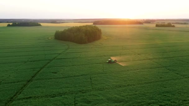 Farm Tractor rocía fertilizantes sobre el campo de cultivos agrícolas contra la puesta del sol — Vídeo de stock