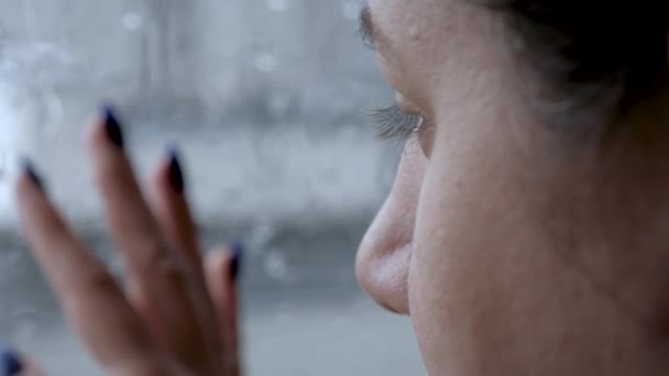 Triste mujer looks en calle bajo lluvia a través de ventana y pone su mano en vidrio — Vídeos de Stock