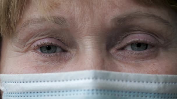 Nahaufnahme von den traurigen Augen einer älteren Frau in einer Schutzmaske auf ihrem Gesicht — Stockvideo