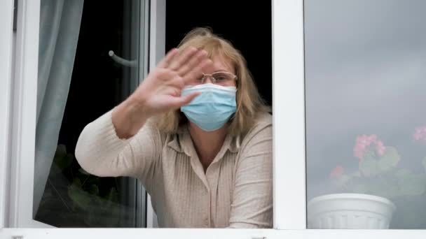 Kobieta w masce medycznej pożegnanie lub powitanie z okna domu w izolacji — Wideo stockowe