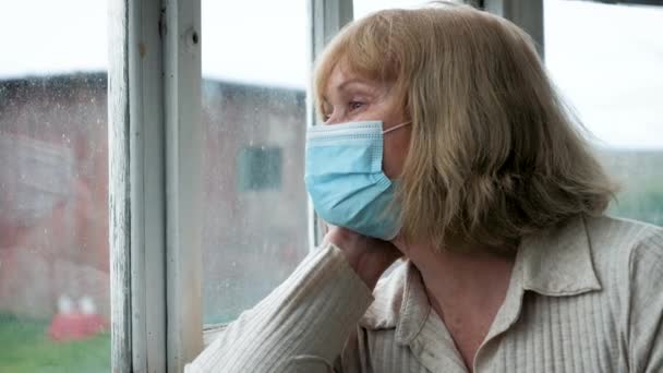 Elderly Woman In Medical Mask Looks Hopelessly Out Of Window At Self Isolation — Stok Video