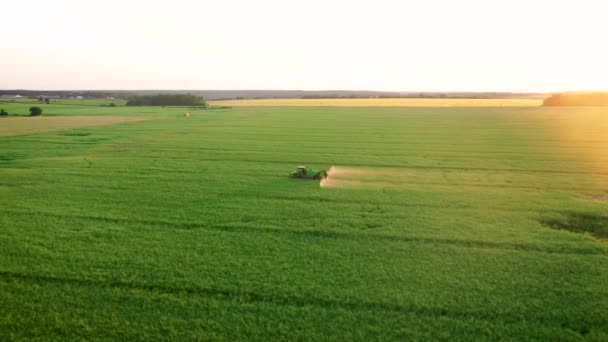 Traktor släpvagn sprutar gödselmedel på åkern av jordbruksgrödor mot solnedgång — Stockvideo