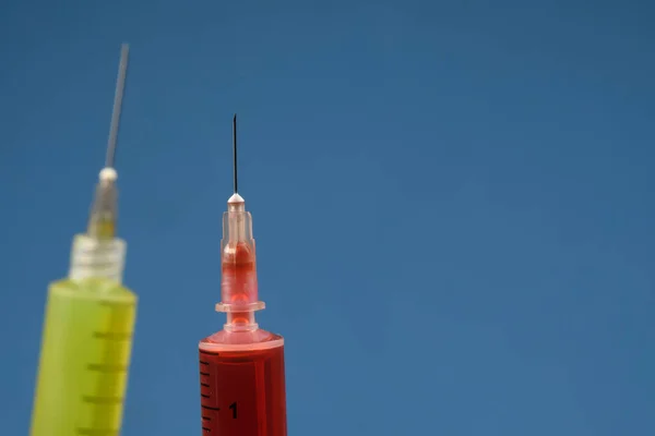 injection syringe with needle detail on colored background with space for text and a defocused syringe yellow