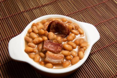 Kariyoka fasulyeli seramik tencere (feijoada) masa üzerinde hasırlı ve kumaş manzaralı.