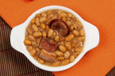 Kariyoka fasulyeli seramik tencere (Feijoada) masa üzerinde hasırlı ve üst görünümde kumaşlı