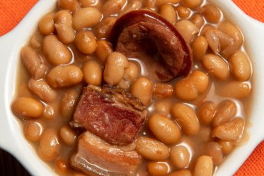 Kariyoka fasulyeli seramik tencere (feijoada) masa üzerinde hasırlı ve üst görünümde kumaşlı.