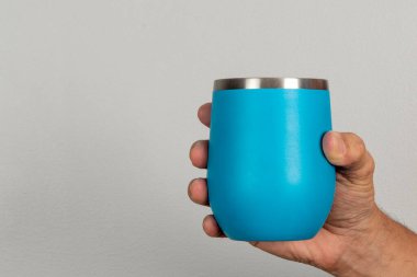 Erkek eli, tarafsız bir arkaplanda mavi bir kupa tutuyor.