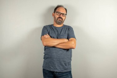 Tişörtlü sakallı bir işçi tarafsız arkaplanda kameraya bakıyor ve duvara yaslanıyor.