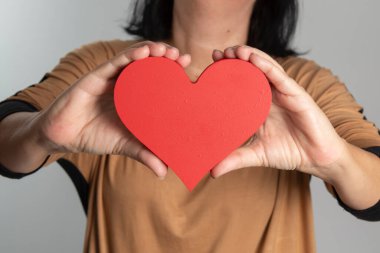 Boynunun önünde kalp tasarımı tutan bir kadın.