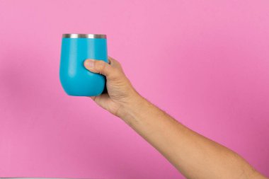 Erkek eli pembe arka planda mavi bir kupa tutuyor.