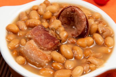 Kariyoka fasulyeli seramik tencere (feijoada) masa üzerinde hasırlı ve kumaş manzaralı.