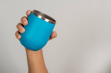 Erkek eli, tarafsız bir arkaplanda mavi bir kupa tutuyor.