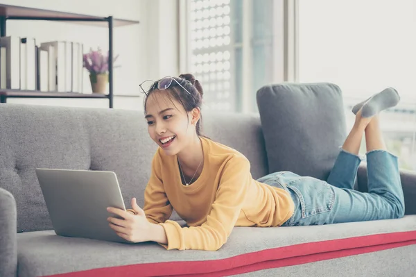 美丽的年轻亚洲女人躺在客厅的沙发上 用电脑笔记本电脑交谈视频电话会议 — 图库照片