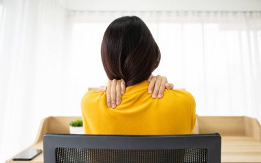 Ofis sendromu konsepti. Bilgisayarda uzun süre çalıştıktan sonra boyun ve omuz ağrısı çeken Asyalı genç bir kadın.