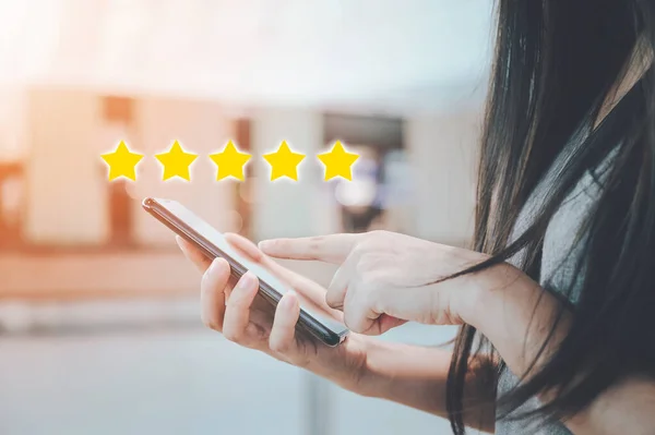 Customer service experience and business satisfaction survey. Close-up image of woman hand using mobile smart phone with icon five star symbol to increase rating of company concept