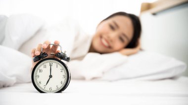 Günaydın yeni gün. Güzel Asyalı kadın mutlu ve zinde uyanır. Beyaz yatak odasında, yatakta gülümsüyor.