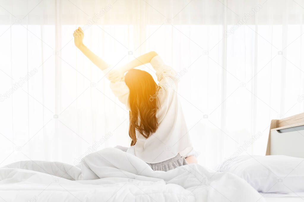 Good morning new day. Asian woman wake up and sitting body stretch on bed beside window in bedroom