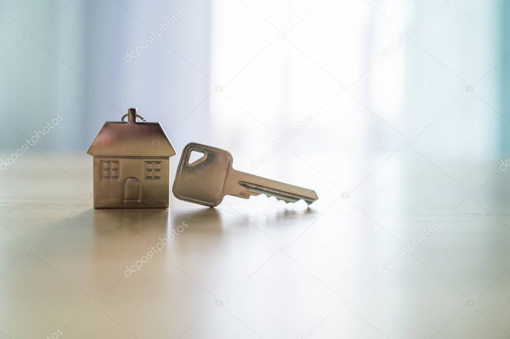 Key and a keychain shaped house on wooden table in room. Property investment and house mortgage financial real estate concept