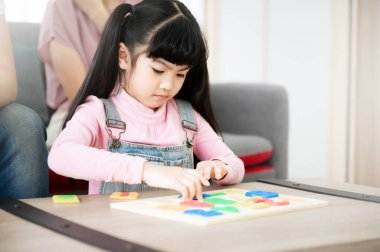 Ailesi evde oyuncak bulmaca oynayan Asyalı bir kız. Küçük kız gülümsüyor ve boş vakitlerin tadını çıkarıyor.