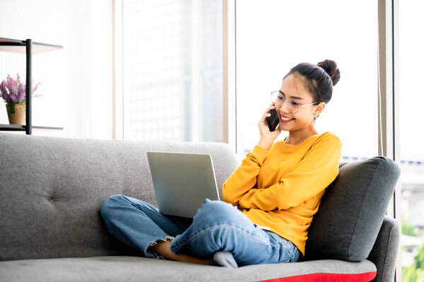 Young asian woman using mobile smartphone and working on laptop at house. Concept of work at home