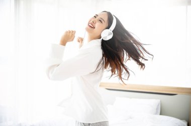 Kulaklıklı, güzel Asyalı bir kadın. Sabah yatak odasında müzik dinliyor ve dans ediyor.