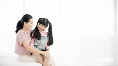 İyi bir kız ve annesi birlikte eğleniyorlar. Evde iyi eğlenceler. Çocuk uykudan uyanıyor. Yatak odasındaki yatakta oynayan Asyalı bir aile.