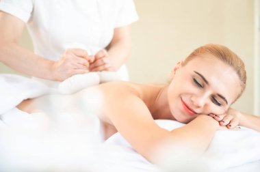Sağlık ve Tayland masajı. Güzel bir kadın Thai bitkisel top kompresi yaptırıyor ve spa salonunda omuz masajı yaptırıyor.