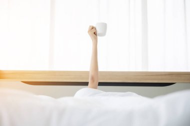 Sabahları yatakta uyanan bir kadın. Battaniyenin altına saklanıyor ve bir fincan kahveyle kollarını açıyor.