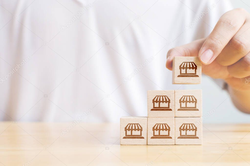 Franchise business marketing system concept. Structure service store network strategy. Hand putting wooden block on top with icon store