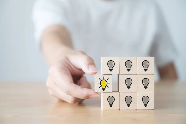 Conceptual of creative idea and innovation. Hand picked wooden cube block with light bulb icon