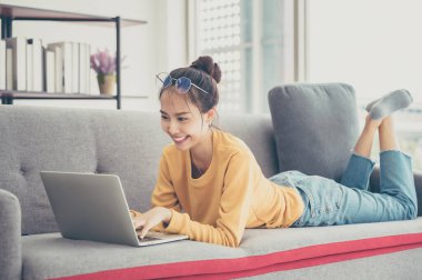 Oturma odasındaki kanepede bilgisayar kullanan Asyalı güzel bir kadın.