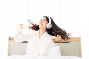 Kulaklıklı, güzel Asyalı bir kadın. Sabah yatak odasında müzik dinliyor ve dans ediyor.