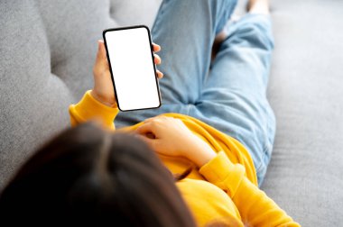 Görüntüyü beyaz ekran mobil akıllı telefona dönüştür. Akıllı telefon kullanan ve koltukta dinlenen bir kadın. Kırpma yolu cihaz ekranı içeriyor