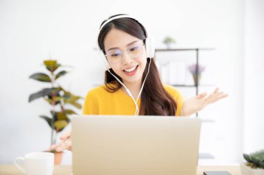 Evde çalışan mutlu genç kız öğrenci, masada oturuyor, dizüstü bilgisayar kullanıyor, görüntülü sohbet ediyor, çevrimiçi ev okulunda öğrenim görüyor.