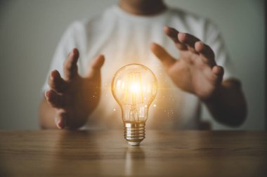 Ahşap masada el ele tutuşan ampul. İlham verici yaratıcı fikir ve gelecekteki teknoloji yeniliği kavramı