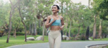 Genç koşucu Asyalı kadın park yolunda koşuyor, spor kıyafetleri ve üst etek giyiyor.
