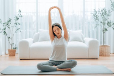 Mutlu genç Asyalı kadın yoga ve omuz egzersizi yapıyor. Oturma odasında yerde oturuyor.