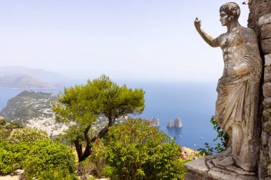 Capri Adası; İtalya - 28 Haziran 2021: Monte Solaro adasının tepesinden Tyrhenian Denizi 'ne Faraglioni kayaları ile hava manzarası; İmparator Augustus' un önplandaki heykeli
