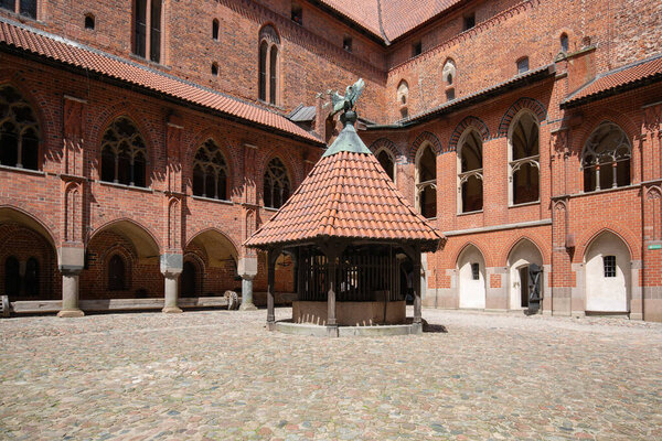 Malbork, Poland - June 25, 2020: Courtyard with well, 13th century Malbork Castle, medieval Teutonic fortress on Nogat River. It is largest gothic castle in world, UNESCO World Heritage Site