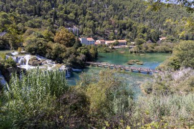 Krka Ulusal Parkı, Hırvatistan - 16 Eylül 2025: Skradinski Buk şelalesi ve yürüyen turistlerle ahşap köprü manzaralı Krka Milli Parkı 