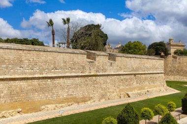 Malta, Mdina - 15 Nisan 2025: Ortaçağ Sessiz Şehri 'ni çevreleyen kireçtaşı şehir duvarları. Etrafında ağaçlar ve çimenler olan güzel bahçeler.