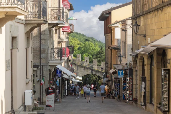 San Marino, San Marino şehri - 10 Haziran 2025: Renkli dükkanlar her iki taraf için de hareketli cadde, insanlar tarihi Porta della Fratta 'ya doğru yürüyorlar. Ortaçağ taş kapısı, eski şehrin ana girişi.
