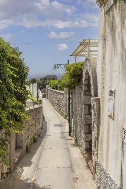 Capri Adası, İtalya - 28 Haziran 2021: Capri 'deki Via Dalmazio Birago' da taş duvarlar ve yeşilliklerle kaplı tipik dar bir sokak, sakin Akdeniz atmosferini yakalıyor.