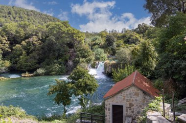 Krka Ulusal Parkı, doğal merak, şelaleler ve Hırvatistan 'daki yeşillikler arasında akan su akıntıları. Kırmızı çatılı eski taş ev.