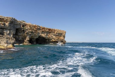 Polignano a Mare, İtalya, Puglia - 24 Mayıs 2024: Adriyatik Denizi üzerindeki resim gibi kayalıklardan manzara. Turistler kayalıklarla mağaraya girerler..