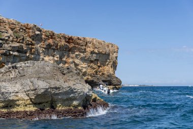 Polignano a Mare, İtalya, Puglia - 24 Mayıs 2024: Adriyatik Denizi üzerindeki resim gibi kayalıklardan manzara. Turistler kayalıklarla mağaraya girerler..