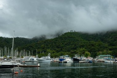 Tekne ve yatlarla dolu sakin bir marina sisli orman tepelerinin altında dinleniyor. Durgun sulardaki huzuru yansıtıyor, Trinidad ve Tobago.