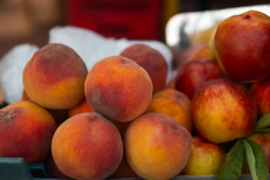 Canlı kırmızı-sarı renkli taze şeftaliler ve nektarlar bir araya toplanmış, yeşil yapraklar ve piyasa dokularıyla vurgulanmış.