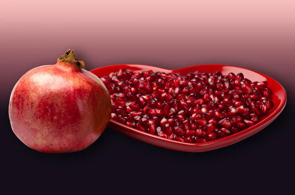 Red heart shaped plate full of delicious ripe juicy pomegranate seeds whole fruit gradient background